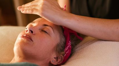 Relaxed woman with closed eyes lying under blanket while getting reiki therapy treatment from unrecognizable therapist in cozy salon with blurred background